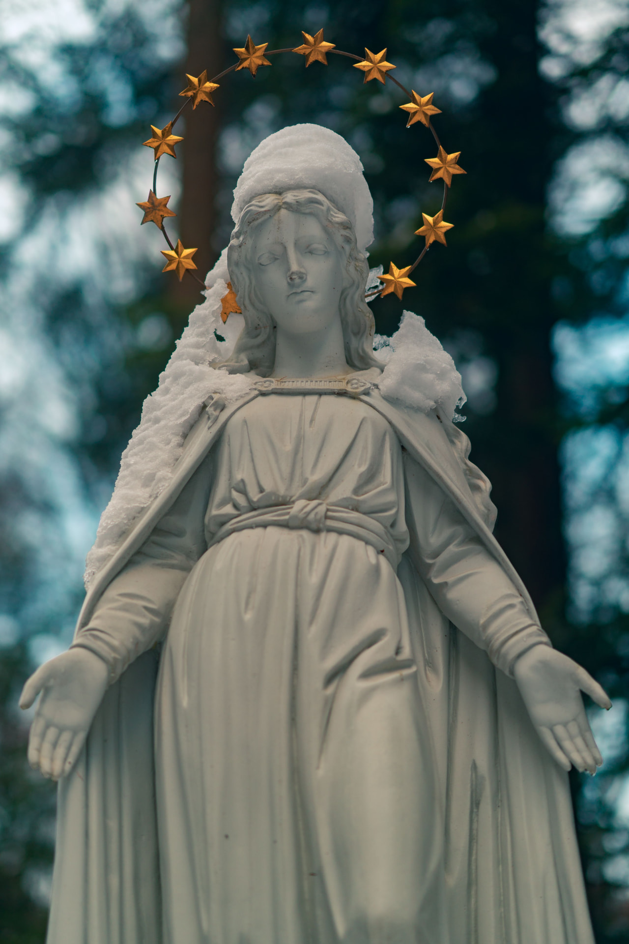 Staty av Maria täckt av snö, med armarna utsträckta och en ring av gyllene stjärnor runt huvudet